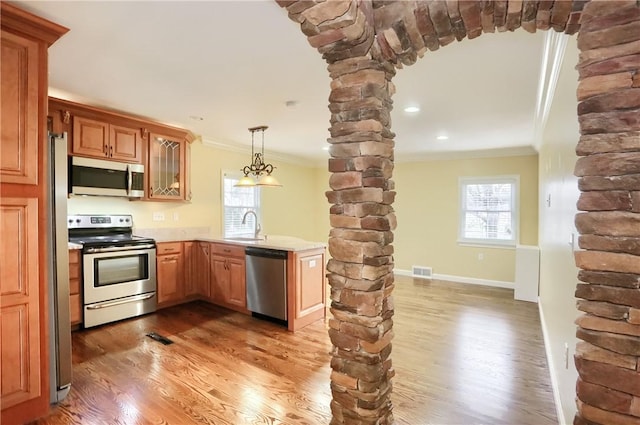 kitchen with sink, hardwood / wood-style floors, decorative light fixtures, appliances with stainless steel finishes, and ornamental molding