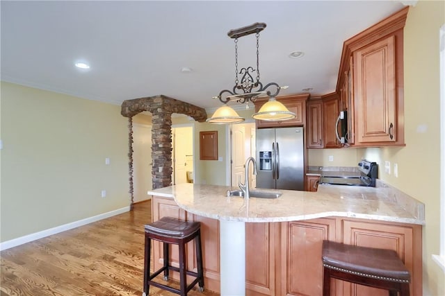 kitchen with ornate columns, sink, kitchen peninsula, appliances with stainless steel finishes, and light wood-type flooring