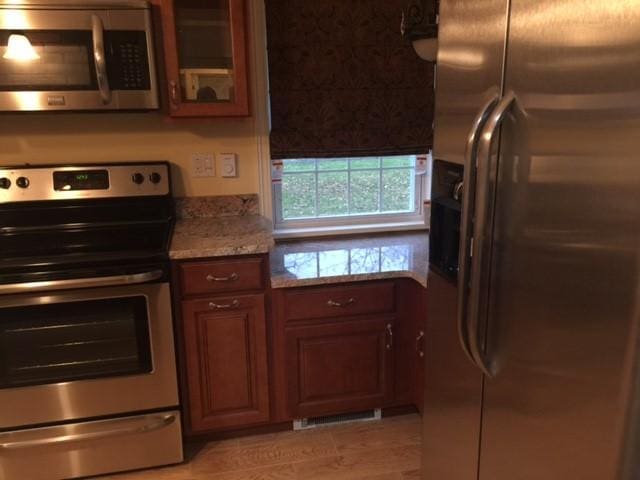 kitchen with stone countertops, appliances with stainless steel finishes, and light hardwood / wood-style flooring