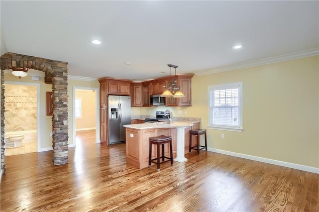 kitchen featuring ornamental molding, a breakfast bar, stainless steel appliances, decorative light fixtures, and hardwood / wood-style flooring