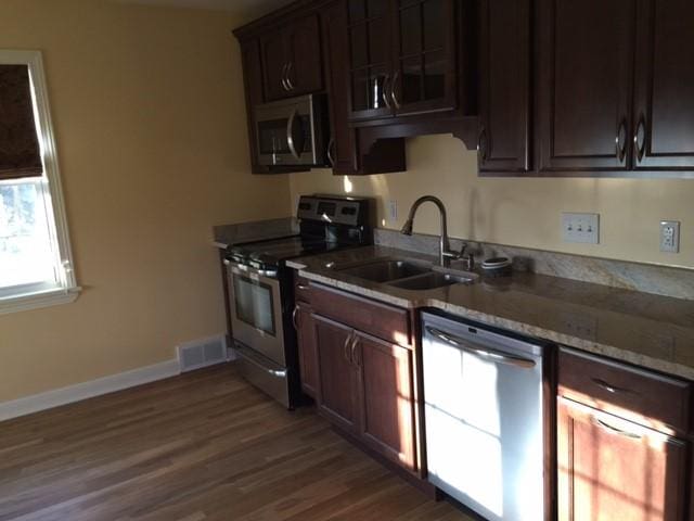 kitchen with sink, dark hardwood / wood-style floors, light stone countertops, appliances with stainless steel finishes, and dark brown cabinetry