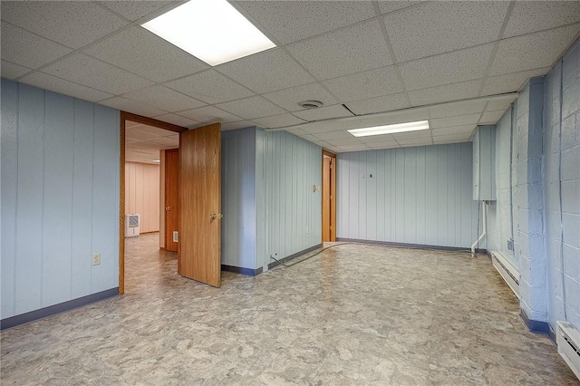 basement with a paneled ceiling, wood walls, and a baseboard radiator