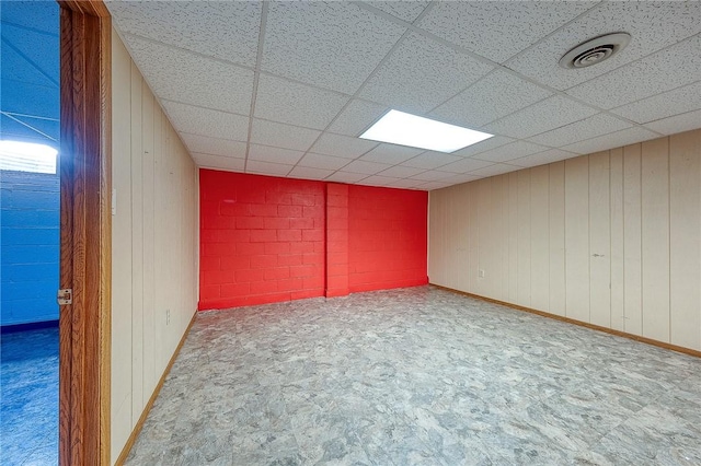 spare room featuring a drop ceiling and wooden walls