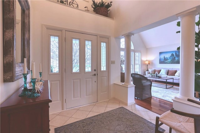 foyer featuring light tile patterned floors, vaulted ceiling, and ornate columns