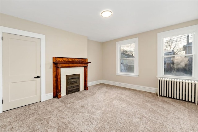 unfurnished living room featuring radiator, a wealth of natural light, light colored carpet, and a tiled fireplace