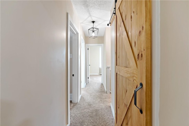 hallway featuring a barn door, light carpet, and a textured ceiling