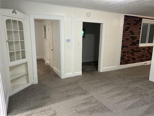 empty room featuring a textured ceiling, dark carpet, and brick wall