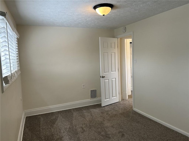 empty room with dark colored carpet and a textured ceiling