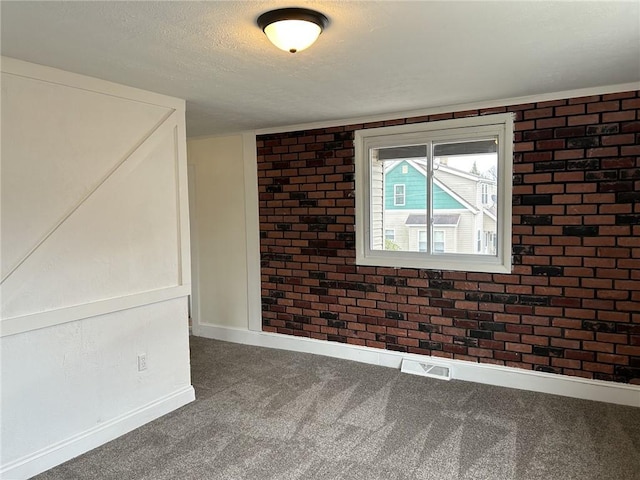 carpeted empty room featuring a textured ceiling and brick wall