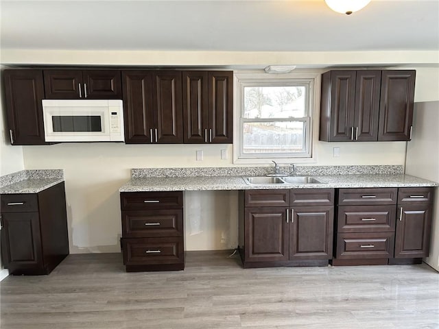 kitchen with dark brown cabinets, light wood-type flooring, and sink