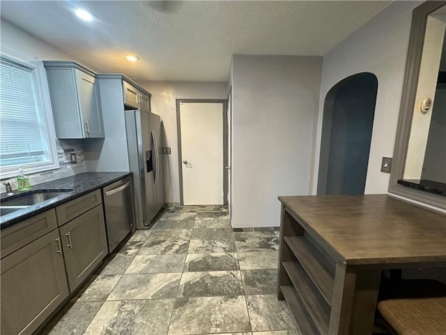 kitchen with gray cabinetry, sink, dark stone countertops, a textured ceiling, and appliances with stainless steel finishes