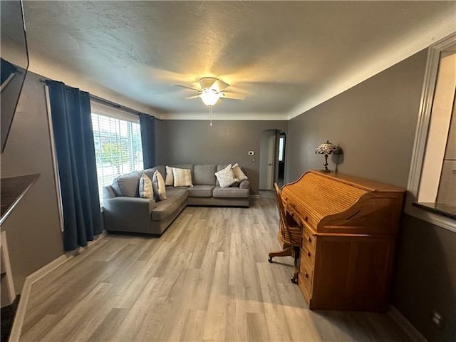 living room with ceiling fan, a textured ceiling, and light wood-type flooring