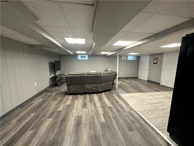 living room with wooden walls, a drop ceiling, and wood-type flooring