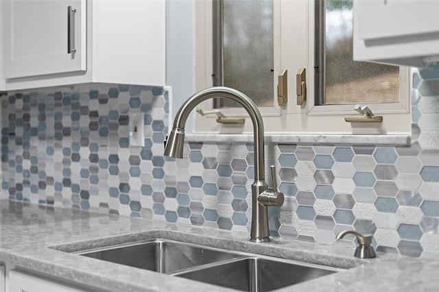 details featuring backsplash, light stone countertops, sink, and white cabinets