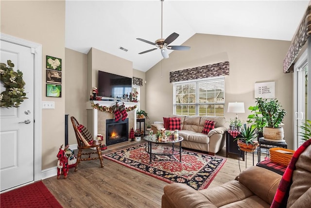 living room with hardwood / wood-style flooring, high vaulted ceiling, ceiling fan, and a tiled fireplace