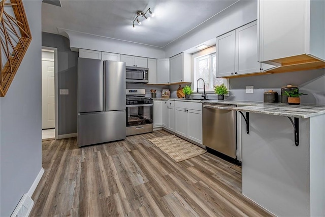 kitchen with sink, appliances with stainless steel finishes, light hardwood / wood-style floors, white cabinetry, and a breakfast bar area