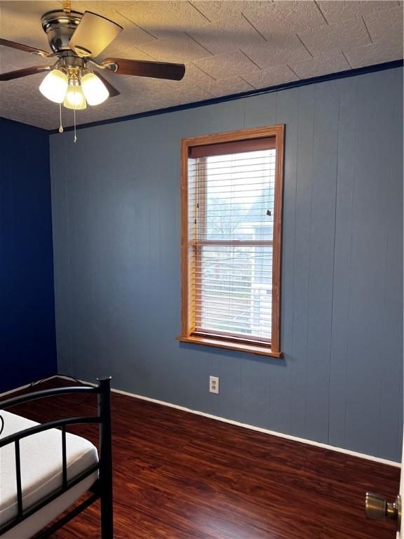 unfurnished bedroom featuring hardwood / wood-style flooring, ceiling fan, wood walls, and multiple windows