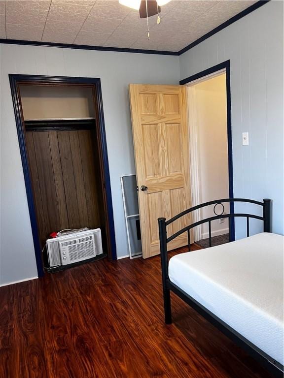 bedroom with dark wood-type flooring, an AC wall unit, wooden walls, a closet, and ornamental molding