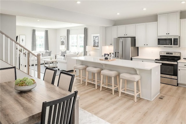 kitchen featuring a breakfast bar, a center island, white cabinets, appliances with stainless steel finishes, and light hardwood / wood-style floors