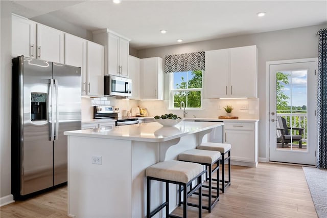 kitchen featuring a kitchen island, white cabinetry, a kitchen bar, decorative backsplash, and stainless steel appliances