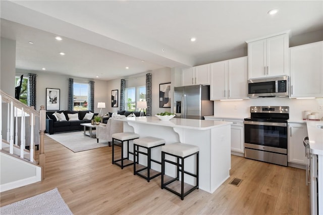 kitchen featuring light hardwood / wood-style flooring, a breakfast bar, appliances with stainless steel finishes, a center island, and white cabinets