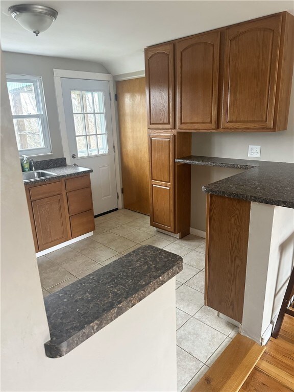 kitchen featuring kitchen peninsula, light tile patterned floors, dark stone countertops, and sink