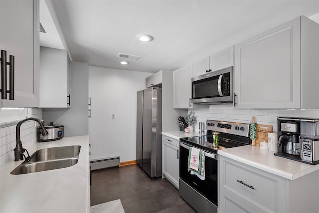 kitchen with backsplash, white cabinets, sink, baseboard heating, and appliances with stainless steel finishes