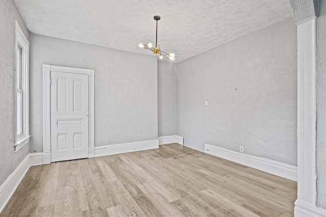 empty room with an inviting chandelier, a textured ceiling, and light hardwood / wood-style flooring