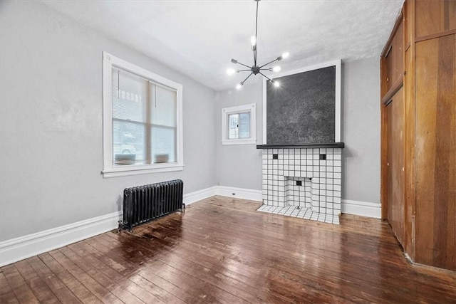 unfurnished living room with a tiled fireplace, radiator heating unit, hardwood / wood-style floors, and a notable chandelier