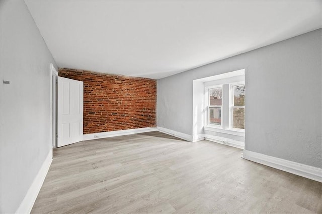 unfurnished room with brick wall and light hardwood / wood-style flooring