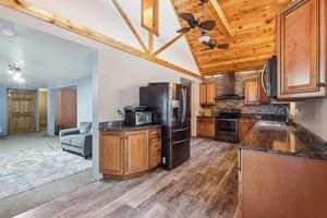 kitchen featuring appliances with stainless steel finishes, wall chimney exhaust hood, ceiling fan, hardwood / wood-style floors, and vaulted ceiling with beams