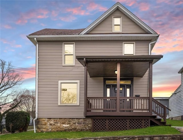 back house at dusk featuring a porch