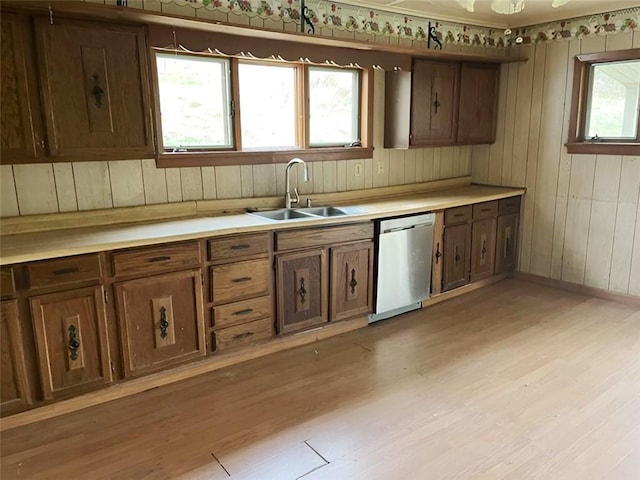 kitchen with sink, dishwasher, wooden walls, and light wood-type flooring