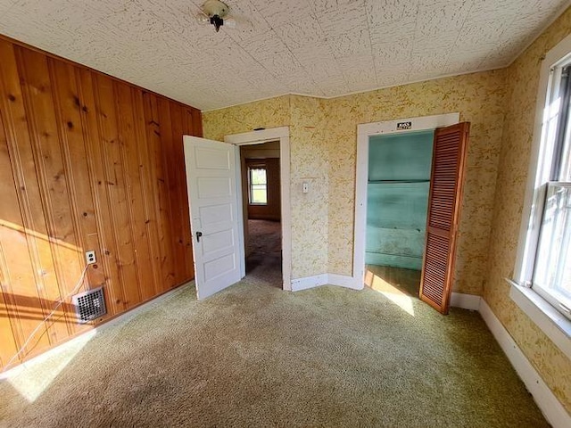 unfurnished bedroom featuring carpet flooring, wooden walls, and multiple windows