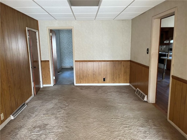 empty room featuring a paneled ceiling, dark carpet, and wood walls