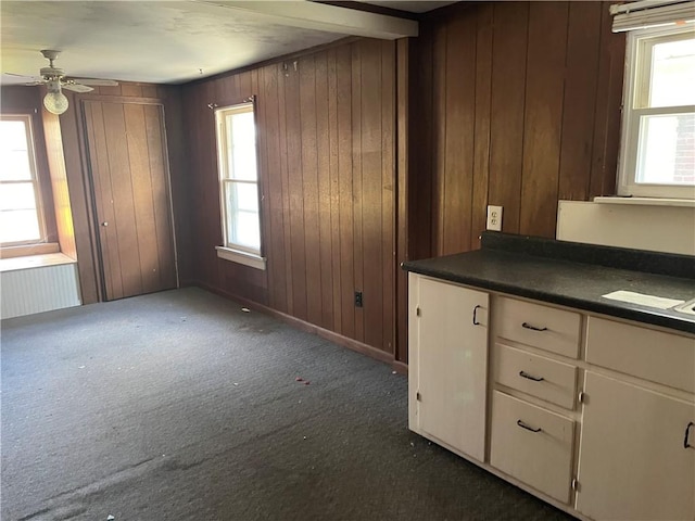 kitchen featuring wooden walls, ceiling fan, and dark colored carpet