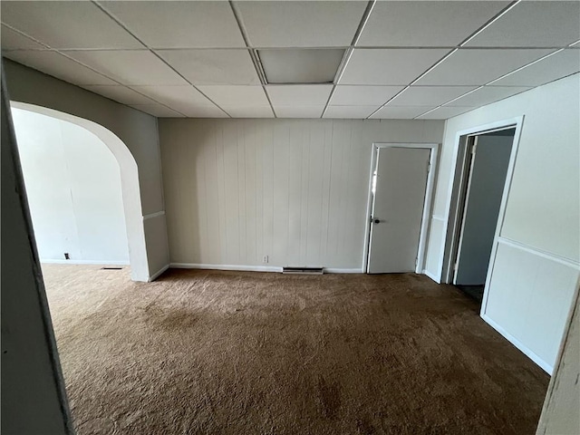 empty room with carpet, a paneled ceiling, baseboards, and arched walkways