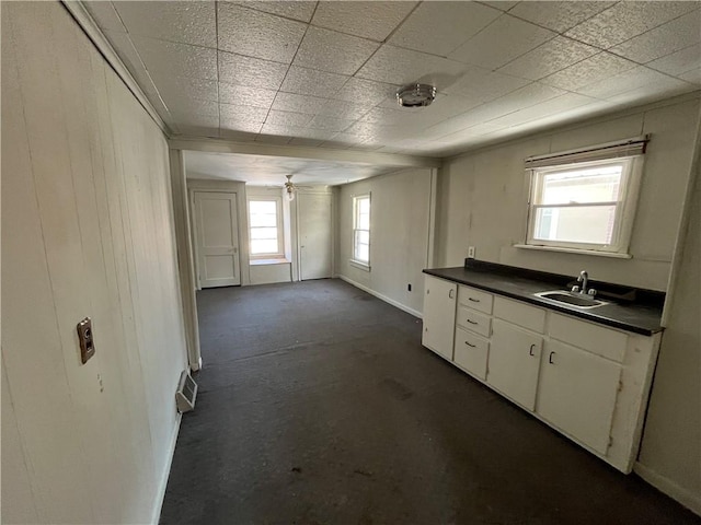 kitchen with white cabinetry, baseboards, dark countertops, and a sink