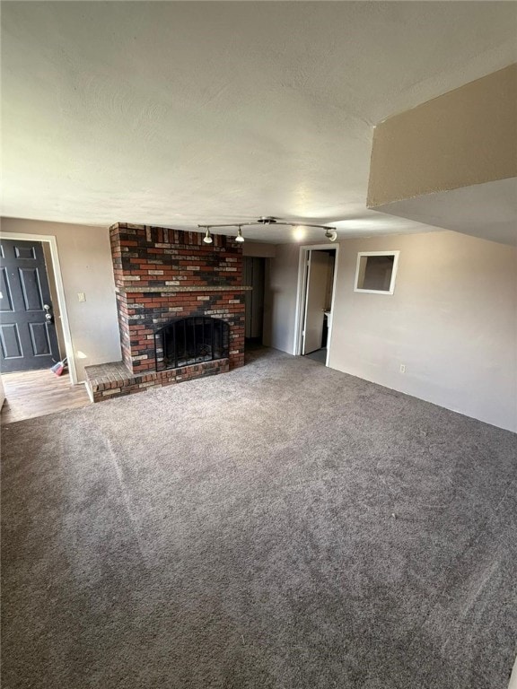 unfurnished living room with carpet floors, track lighting, and a brick fireplace