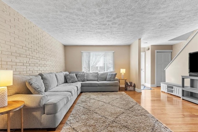 living room featuring brick wall, a textured ceiling, and light wood-type flooring