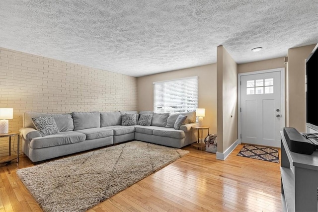 living room with a textured ceiling, brick wall, and light hardwood / wood-style flooring