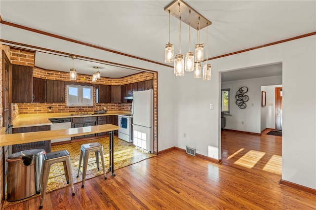 kitchen featuring kitchen peninsula, dark brown cabinets, ornamental molding, and light wood-type flooring