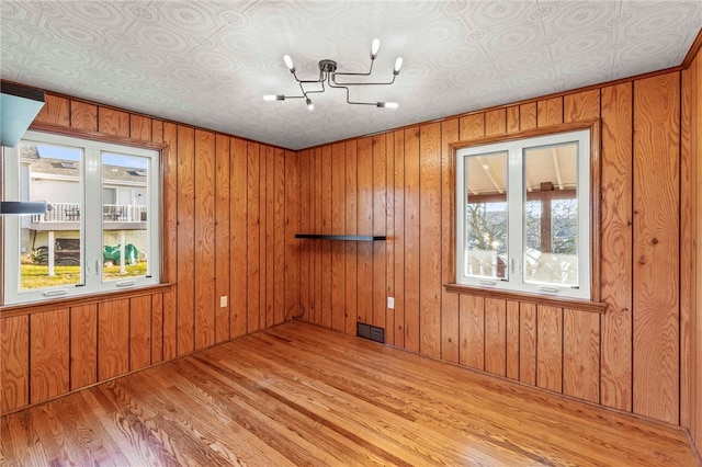 empty room featuring a chandelier, light wood-type flooring, and wood walls