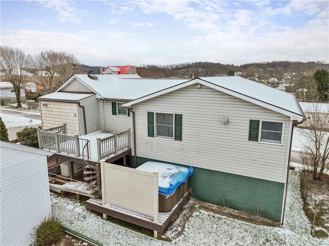 snow covered back of property featuring a hot tub and a wooden deck