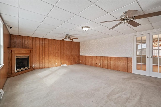 unfurnished living room featuring carpet, wooden walls, ceiling fan, and french doors