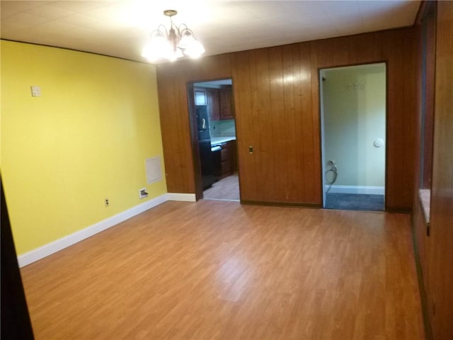 empty room with wood walls, hardwood / wood-style floors, and a chandelier