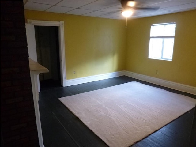 unfurnished room with a paneled ceiling, ceiling fan, and dark hardwood / wood-style flooring