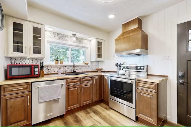 kitchen featuring exhaust hood, wall chimney range hood, sink, light hardwood / wood-style flooring, and appliances with stainless steel finishes