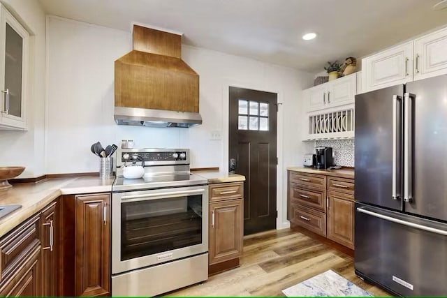 kitchen with white cabinetry, light hardwood / wood-style flooring, wall chimney range hood, and appliances with stainless steel finishes