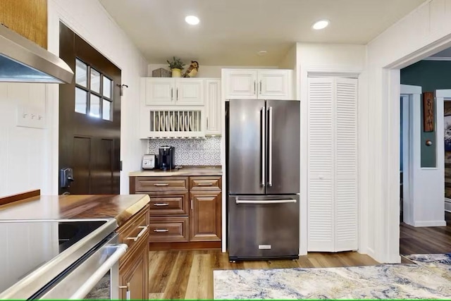 kitchen with backsplash, white cabinets, wall chimney range hood, light wood-type flooring, and stainless steel appliances